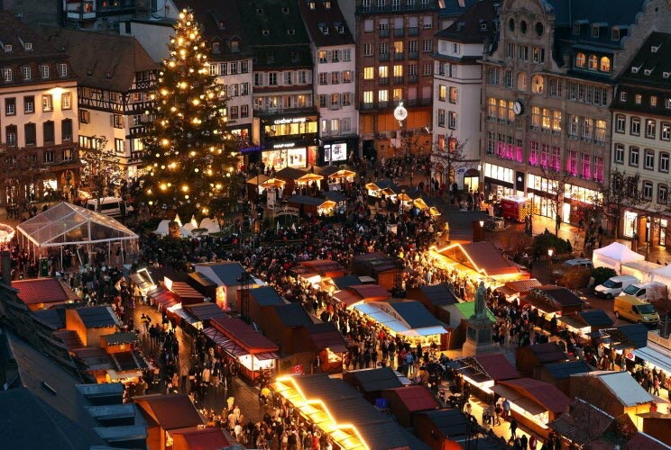 Vue plongeante sur la place Kléber à Strasbourg pendant le marché de Noël : le Grand Sapin illuminé, les toits des chalets et la foule à la nuit tombée